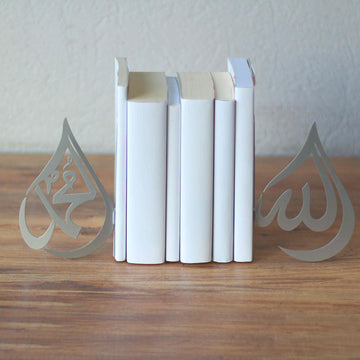 Silberne Buchstützen im Tropfendesign Allah und Mohammed (Friede sei mit ihm) neben weißen Büchern, Weitwinkel auf einem Holztisch