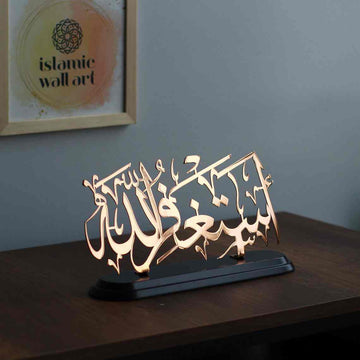 Shiny copper Astaghfirullah calligraphy table decor on a black wooden stand on a dark desk