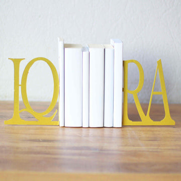 Gold IQRA bookends holding a short row of white books on a wooden table