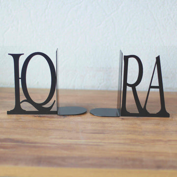 Black IQRA Latin letter bookends standing apart on a wooden table, closer view