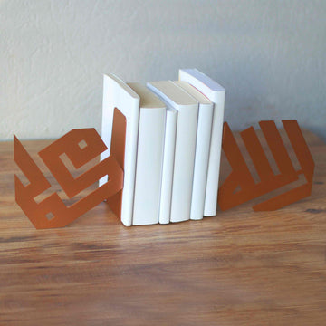 Schrägansicht kupferfarbener kufischer Buchstützen Allah und Mohammed mit einem schräg stehenden Stapel weißer Bücher