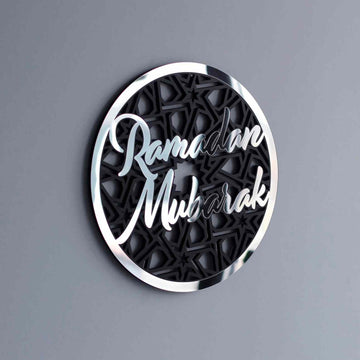 Silver Ramadan Mubarak circular wall decor with script over a black geometric pattern on a gray wall