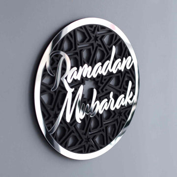Silver Ramadan Mubarak circular wall decor with a polished rim, angled on a gray wall