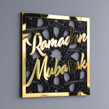 Gold mirror Ramadan Mubarak lettering on a black geometric square wooden wall art, angled on a gray wall