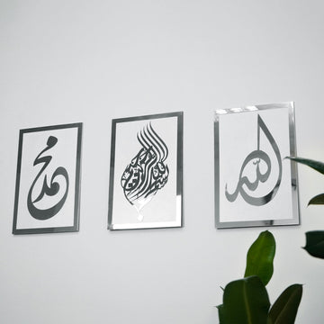 Basmala, Allah and Muhammad wooden wall art set, Silver on White, straight view beside a plant