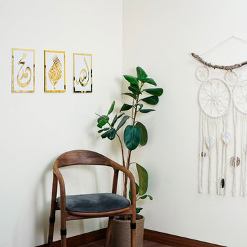 Basmala, Allah and Muhammad wooden wall art set, Gold on White, hung in a corner with a chair and plant