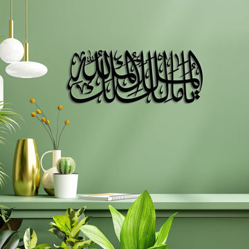 لوحة جدارية معدنية «يا مالك الملك، الملك لله» باللون الأسود على جدار أخضر فوق رف عليه مزهريات